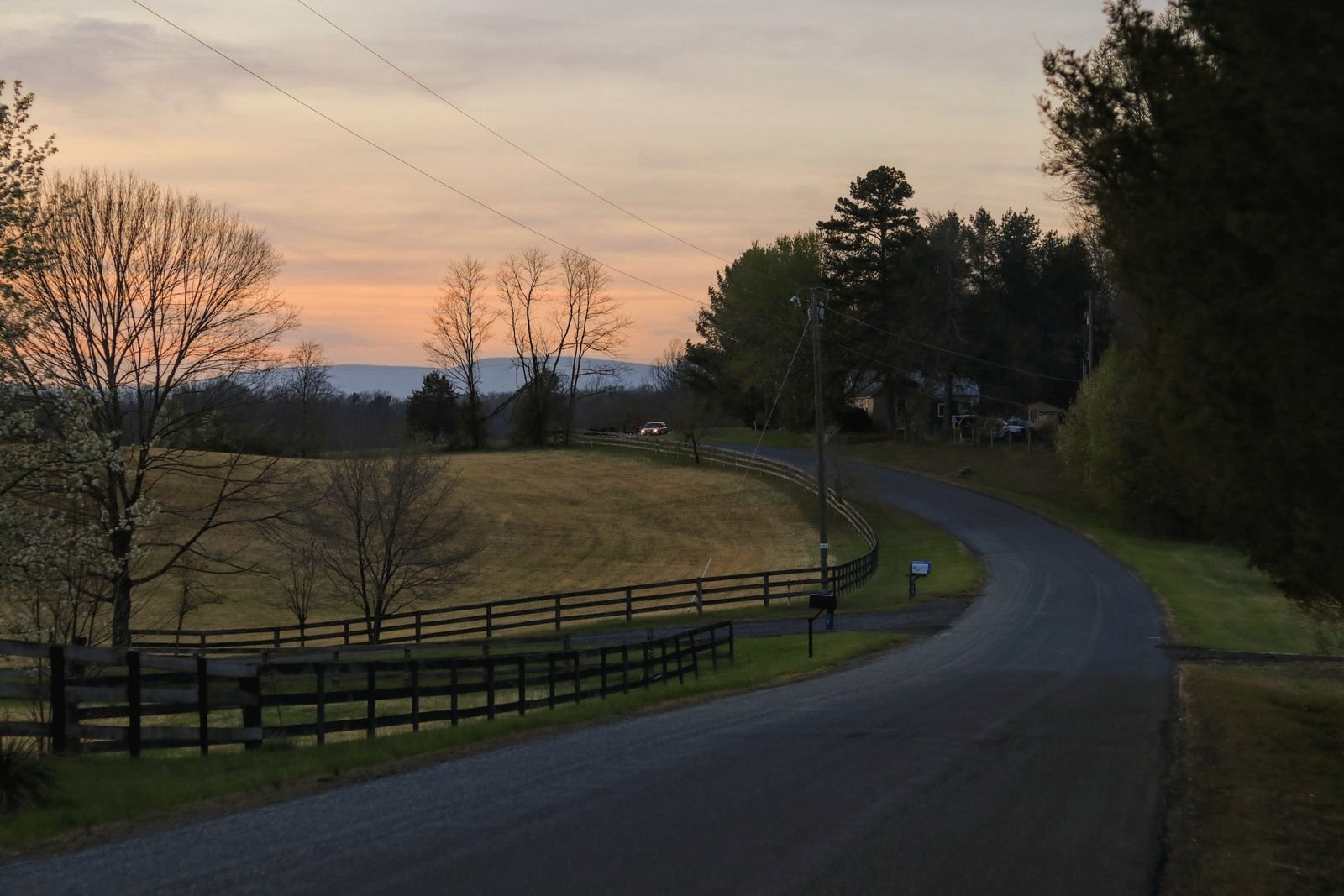 Fenced pasture road at dusk with a wooded ridge on the horizon, the kind of two-lane this part of Georgia is made of