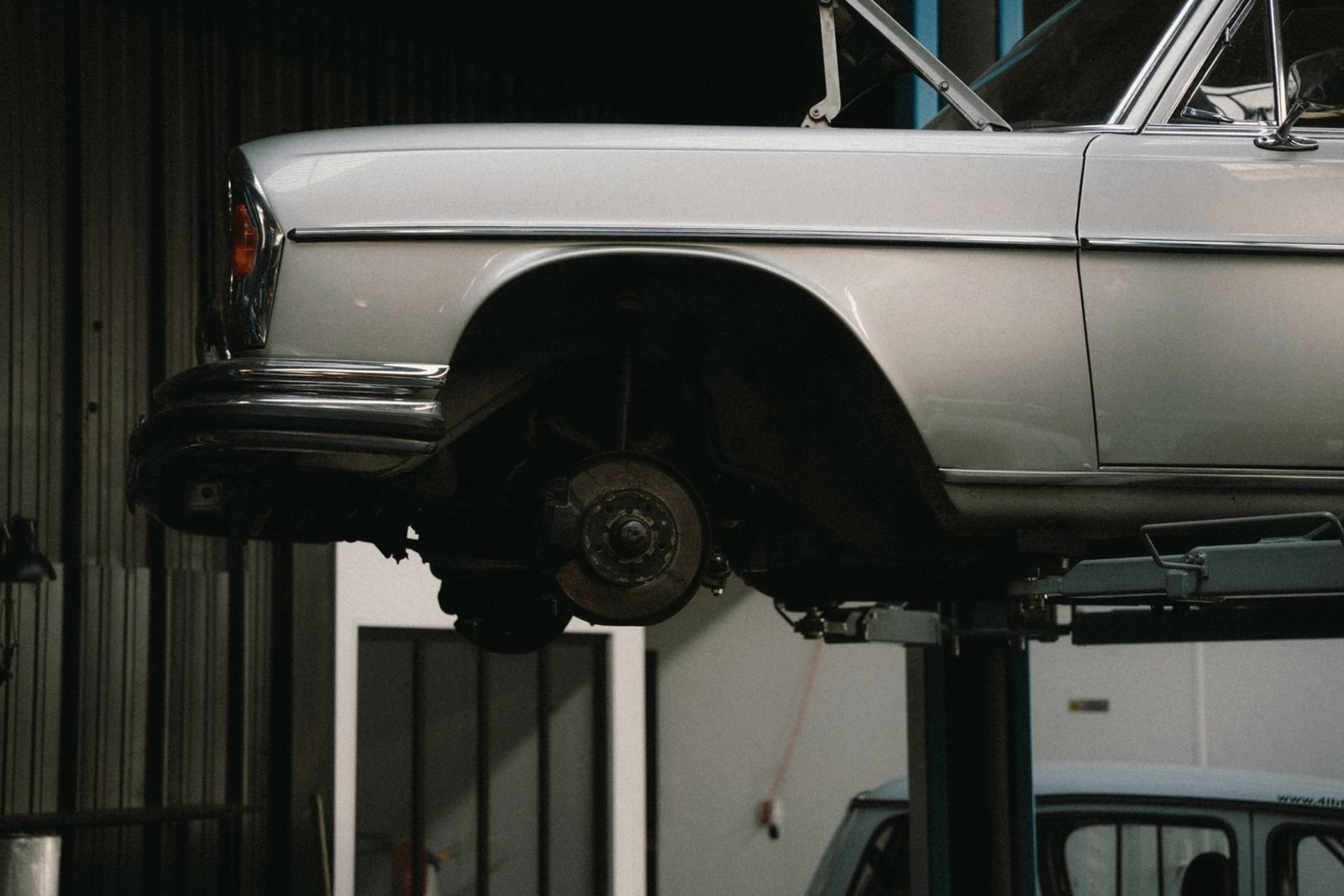 Front quarter of a classic sedan raised on a lift, wheel off, brake rotor exposed