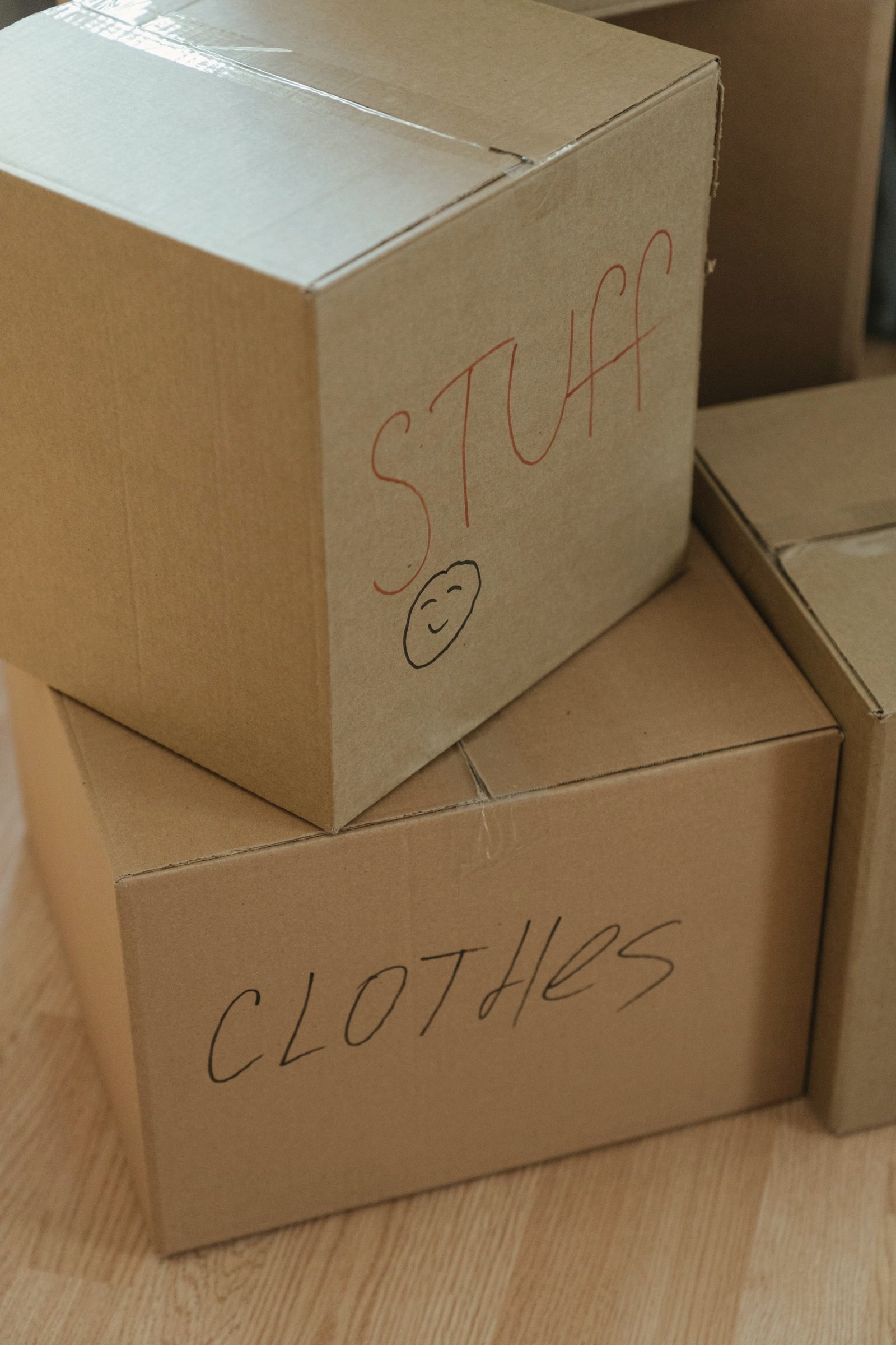 Hand-labeled cardboard moving boxes stacked on a wood floor