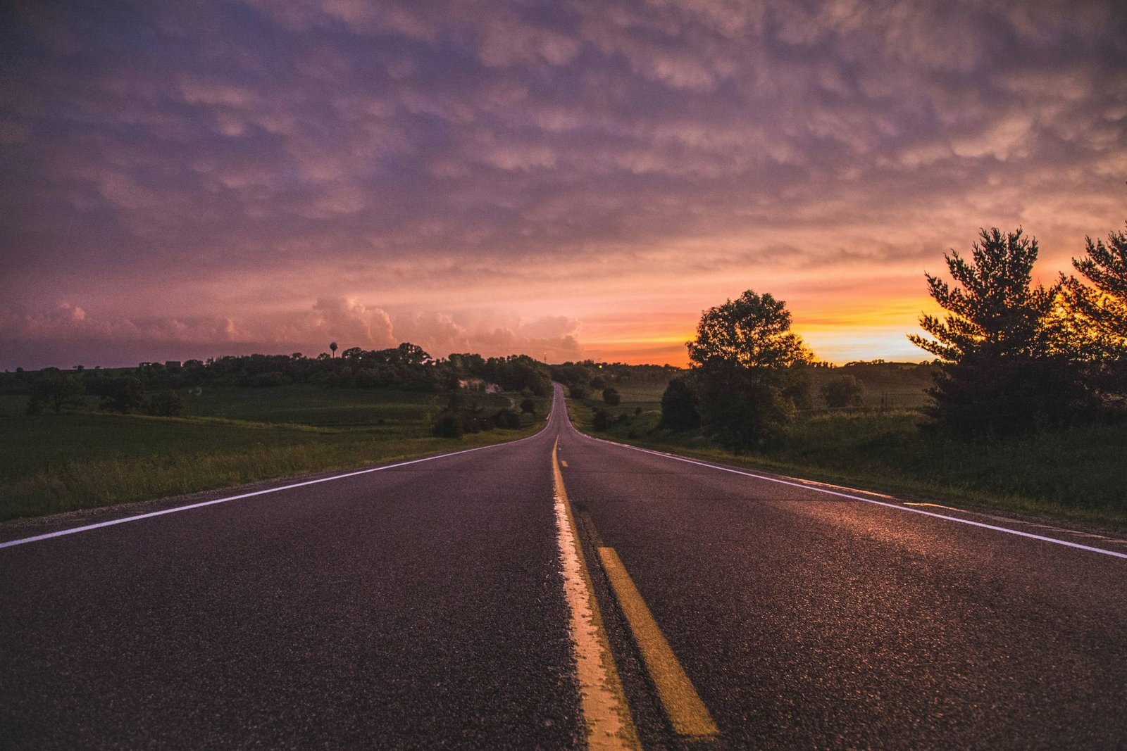 Two-lane country road at dusk under a violet sky, representative of the roads a wrecker works after dark