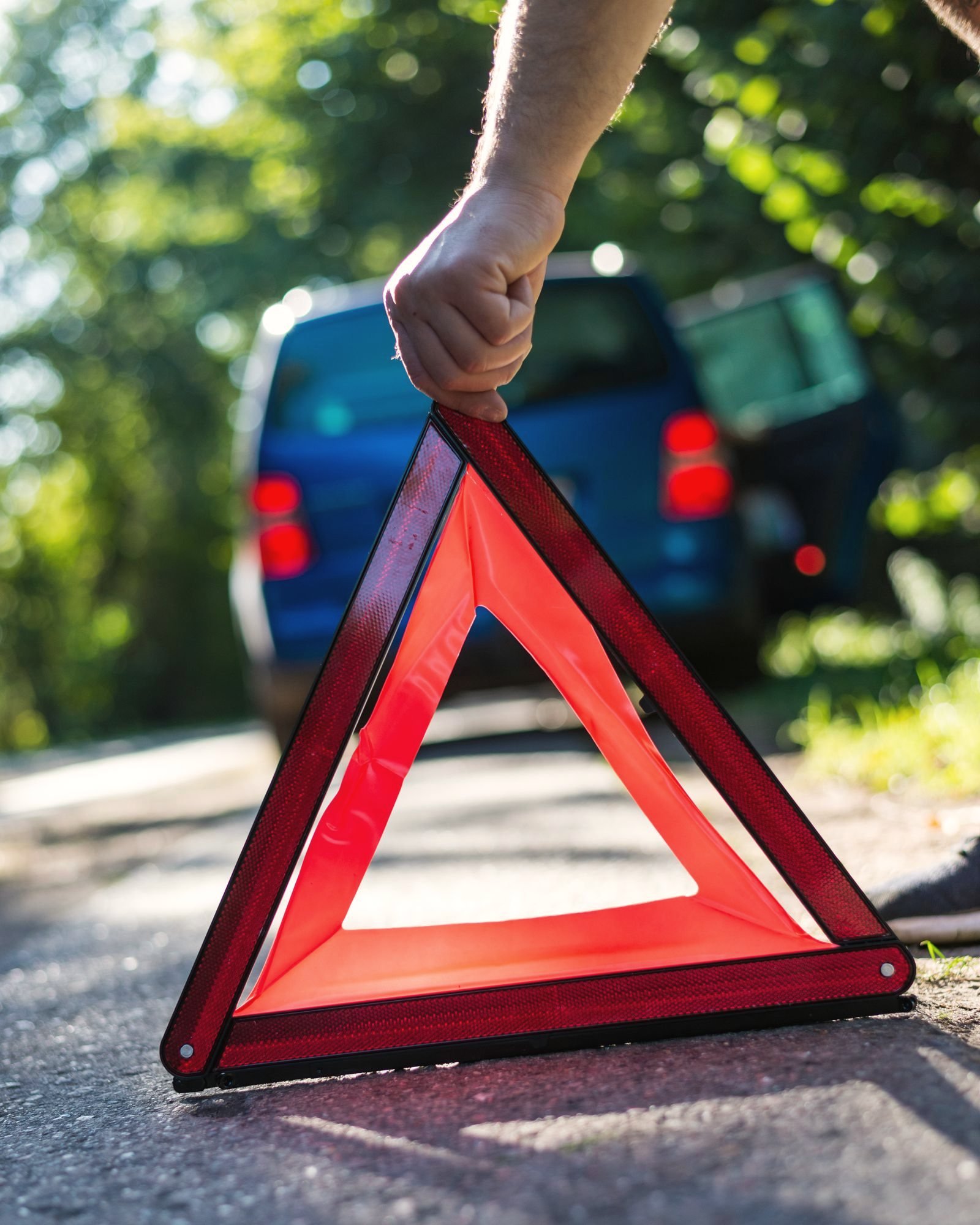 Reflective warning triangle being set on the pavement behind a stopped vehicle