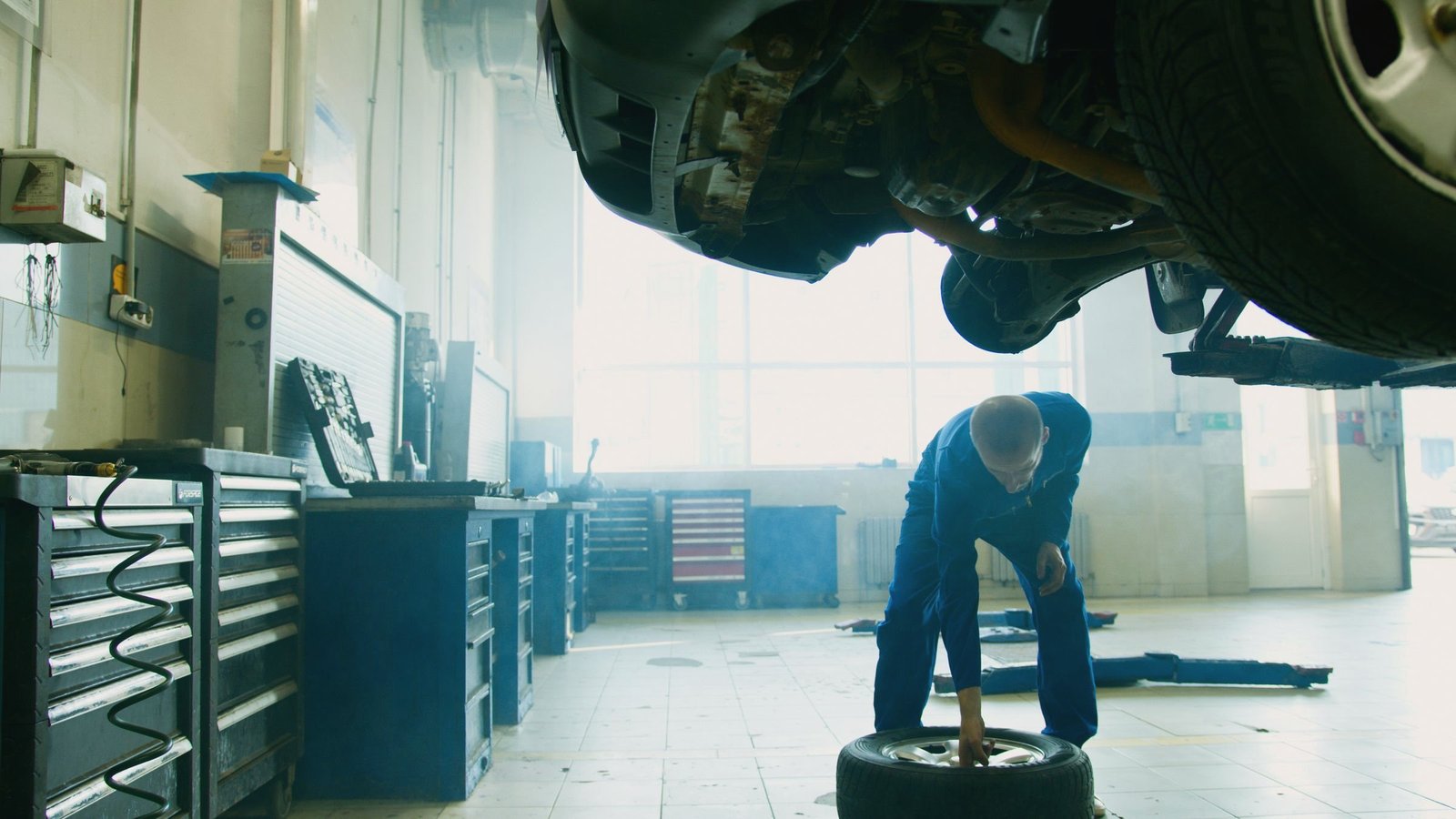 Mechanic working a wheel beneath a car raised on a lift in a daylight service bay