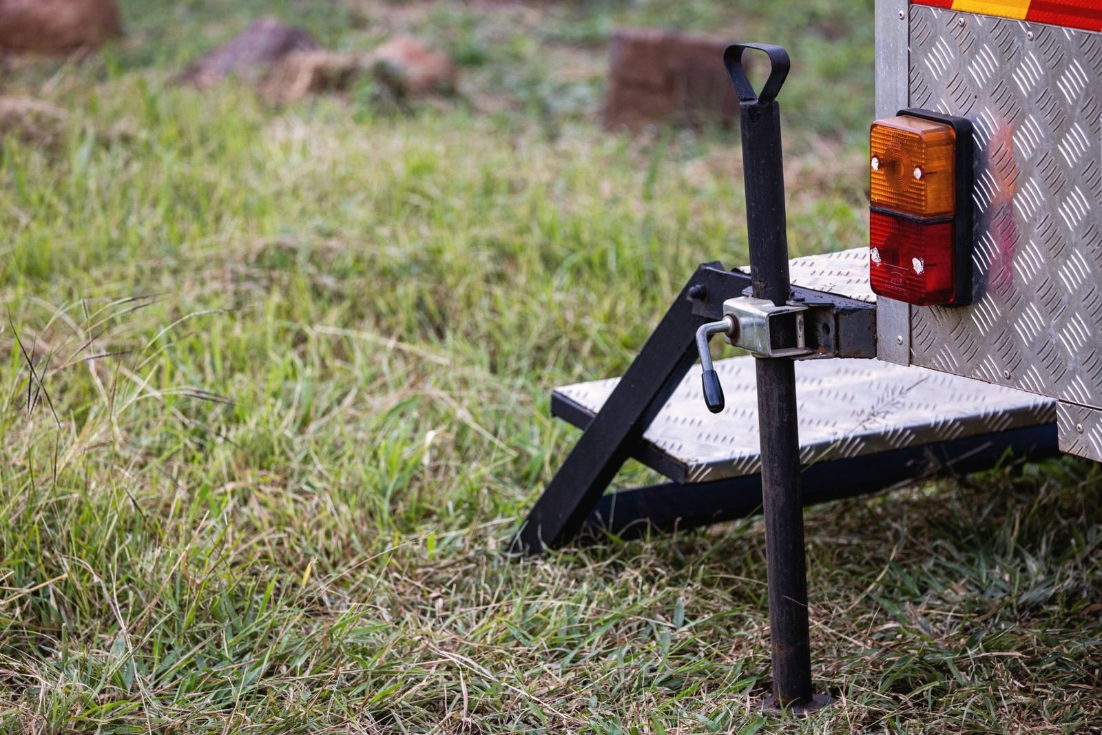 Trailer tongue jack and checker-plate step on a utility trailer parked on grass
